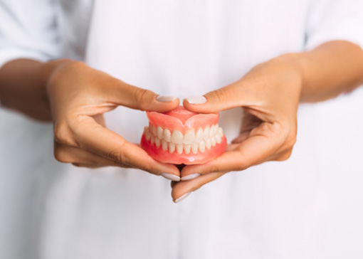 Woman wearing white holding complete set of dentures in front of abdomen