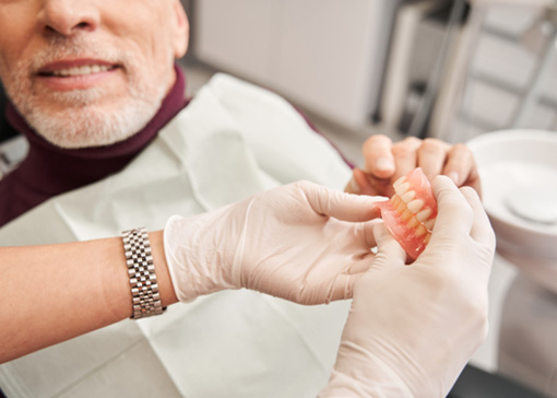 Dentist wearing white gloves handing dentures to patient