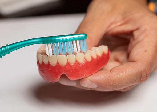 A toothbrush being used to clean a denture