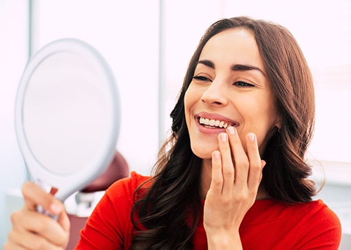 Woman in red-orange shirt admiring reflection in handheld mirror